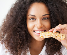 Smiling African woman eating a heathy cereal snack bar.