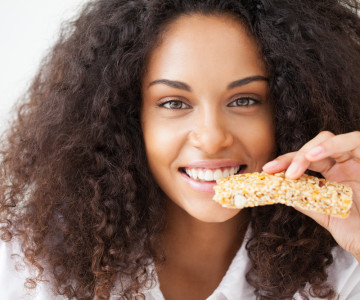 Smiling African woman eating a heathy cereal snack bar.