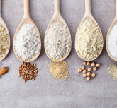 Wooden spoons of various gluten free flour (almond flour, amaranth seeds flour, buckwheat flour, rice flour, chick peas flour) from top view