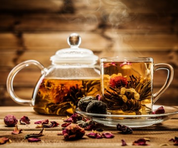 Teapot and glass cup with blooming tea flower inside against wooden background