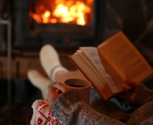 Woman resting with cup of hot drink and book near fireplace
