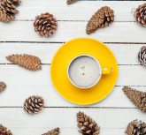 photo of yellow cup of coffee near dried beautiful cones on the wonderful white wooden background
