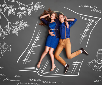 Happy valentines love story concept of a romantic couple on a picnic sharing headphones and listening to the music against chalk drawings background.